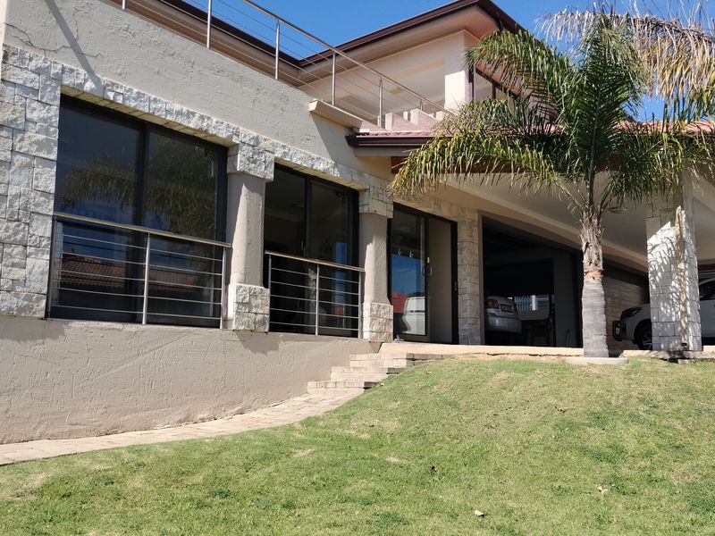 Rear view of the property featuring stone cladding, sliding glass doors, a covered patio area, and an upper-level balcony with stainless steel railings.
