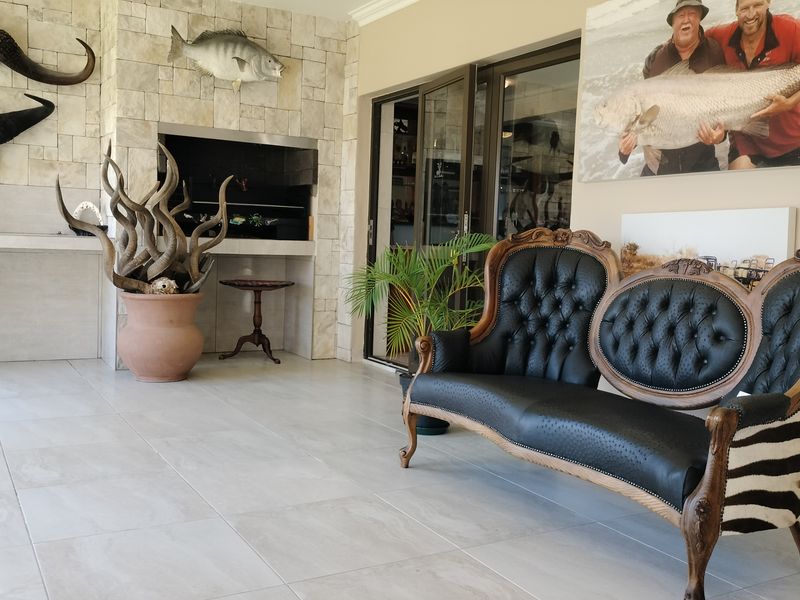 Covered patio area featuring a built-in braai with stone cladding, large format floor tiles, and sliding glass doors leading into the home.