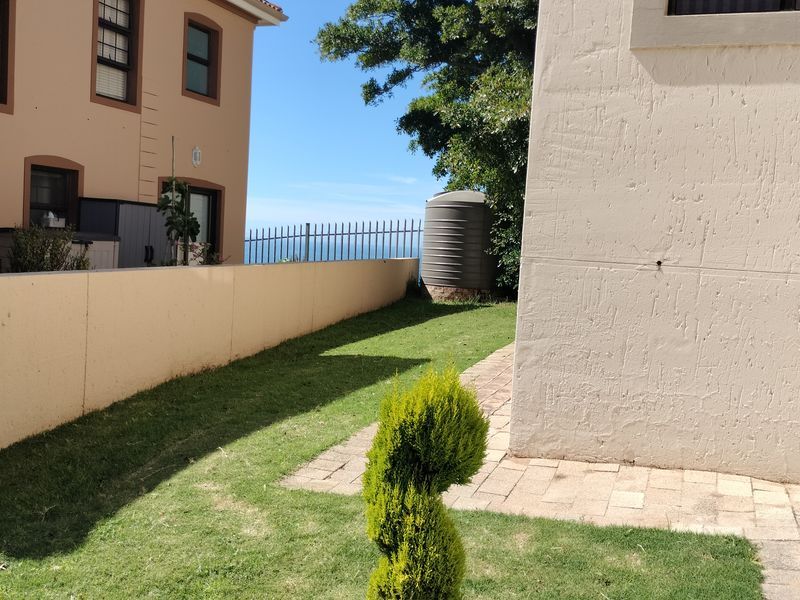Rear garden area featuring a paved walkway, boundary wall, and water tank with views towards the horizon.
