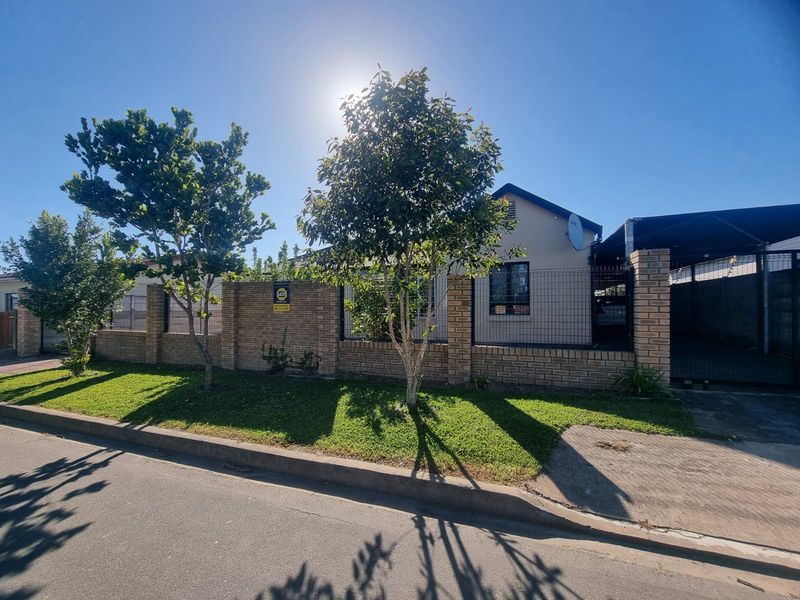 Front exterior view of the property featuring a brick boundary wall, wire mesh fencing, a paved driveway, and a carport.