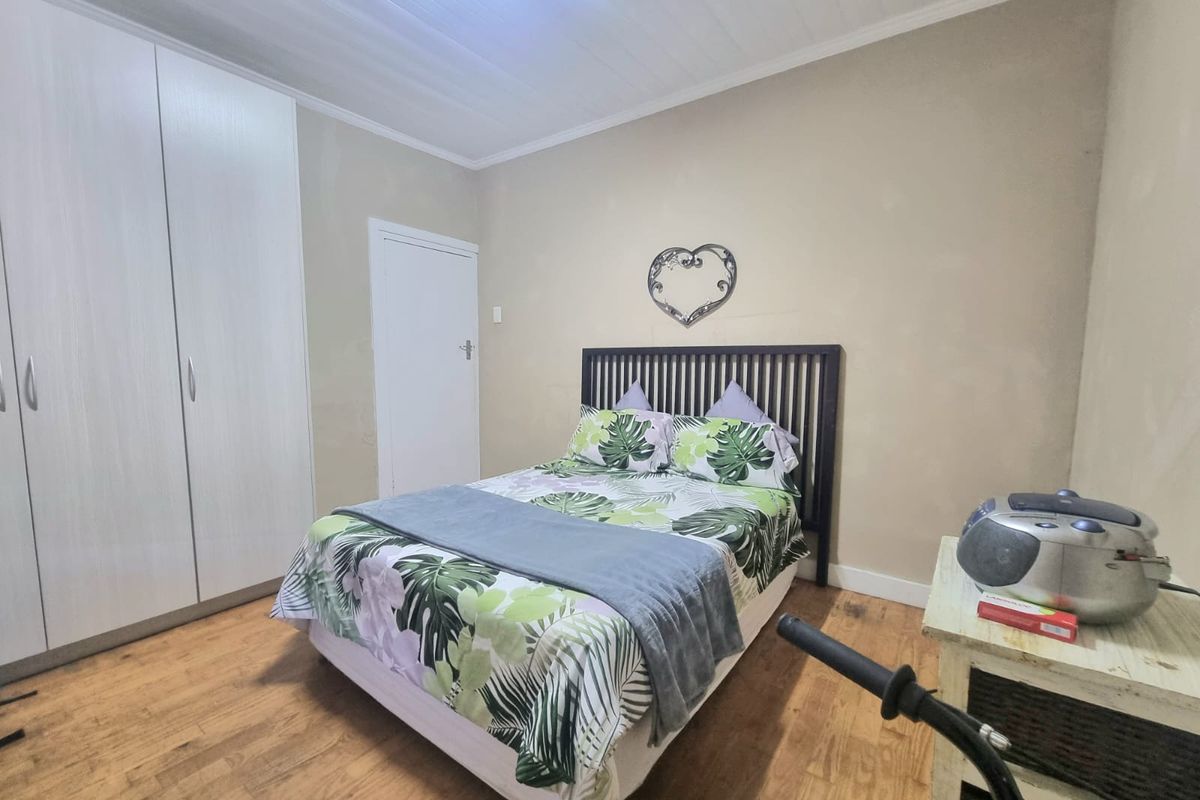 A functional bedroom featuring built-in cupboards, laminated flooring, and a classic tongue and groove ceiling finish.