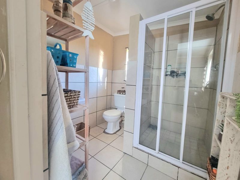 A functional bathroom featuring a tiled shower enclosure, toilet, and neutral wall and floor tiling.