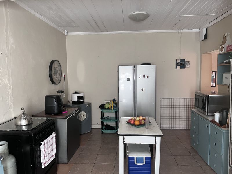 A functional kitchen space featuring tiled flooring, timber ceiling, and basic cabinetry, requiring cosmetic updates to modernize the finishes and improve overall presentation.