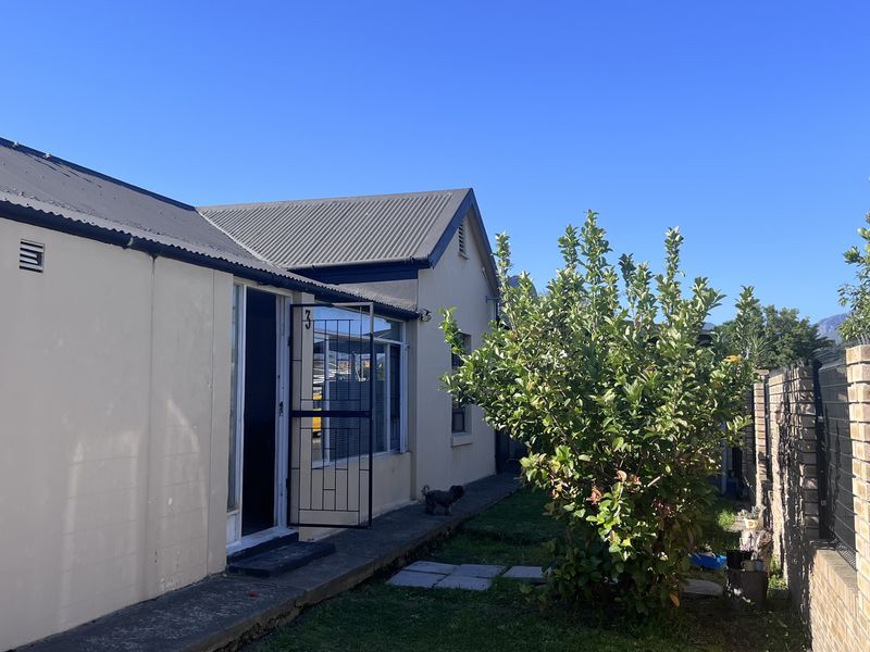 Rear exterior view of the property featuring a corrugated metal roof, concrete pathway, and secure boundary walling with mesh fencing.