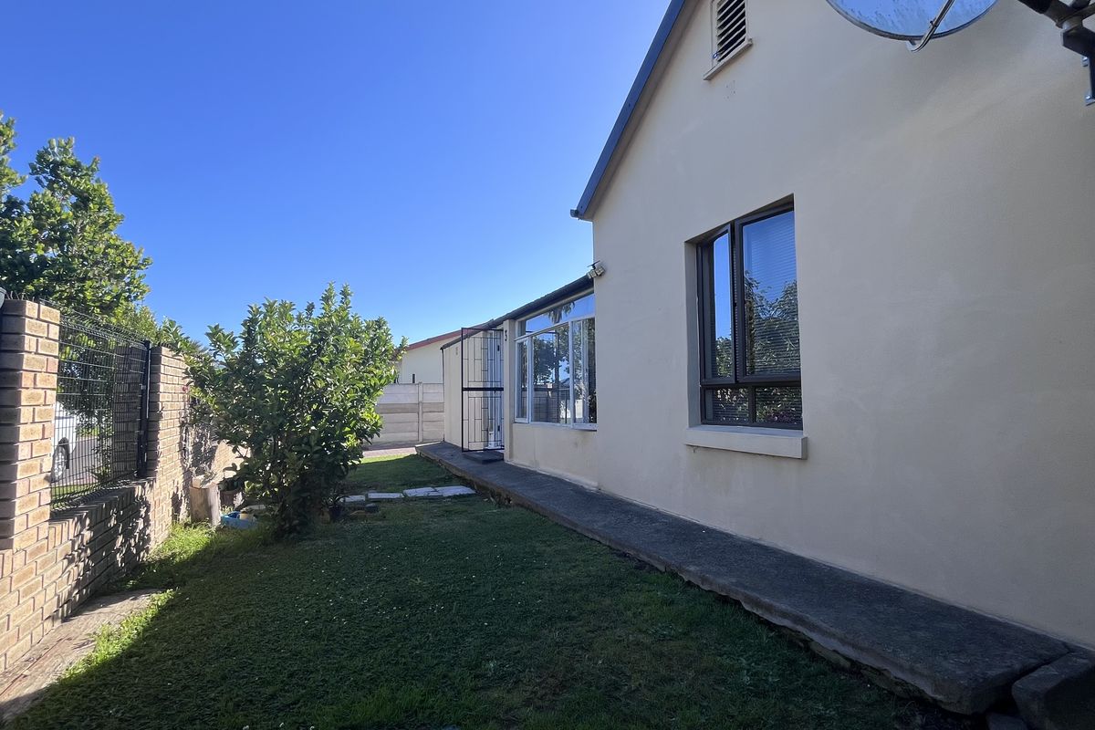 Rear exterior view of the property featuring a concrete walkway, brick boundary wall, and aluminium window frames.