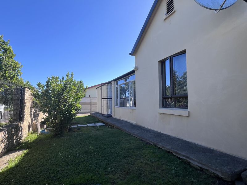 Rear exterior view of the property featuring a concrete walkway, brick boundary wall, and aluminium window frames.