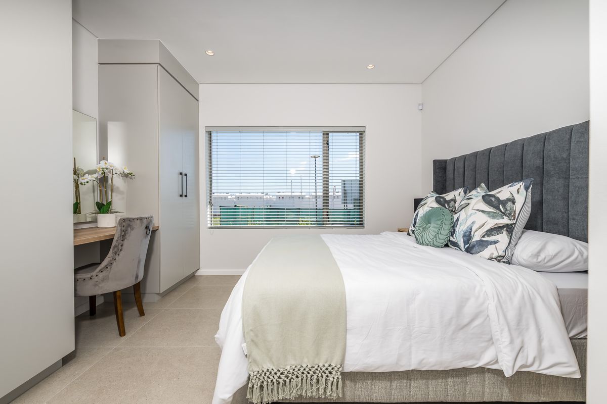 A modern, well-maintained bedroom featuring neutral tiled flooring, built-in cabinetry with an integrated vanity, and recessed ceiling lighting.