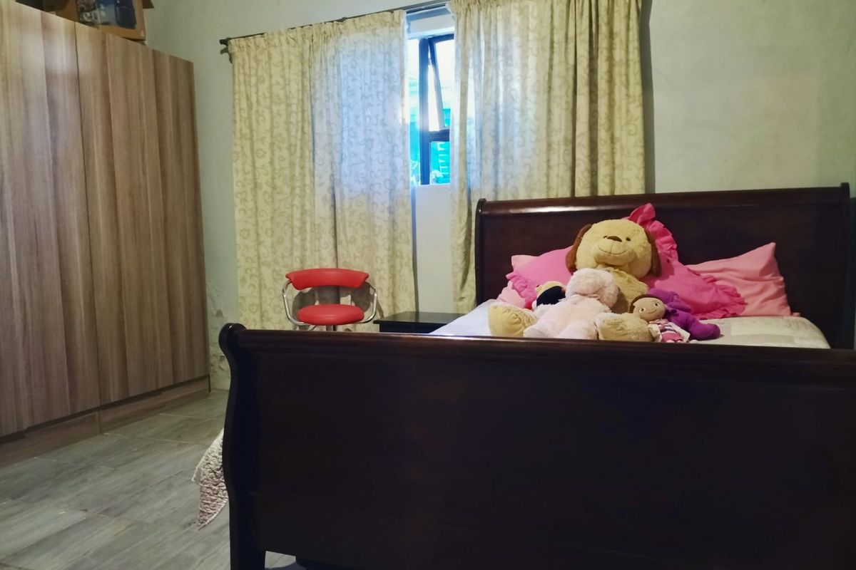 A bedroom featuring tiled flooring, built-in wooden wardrobe, and a window with curtain treatments.