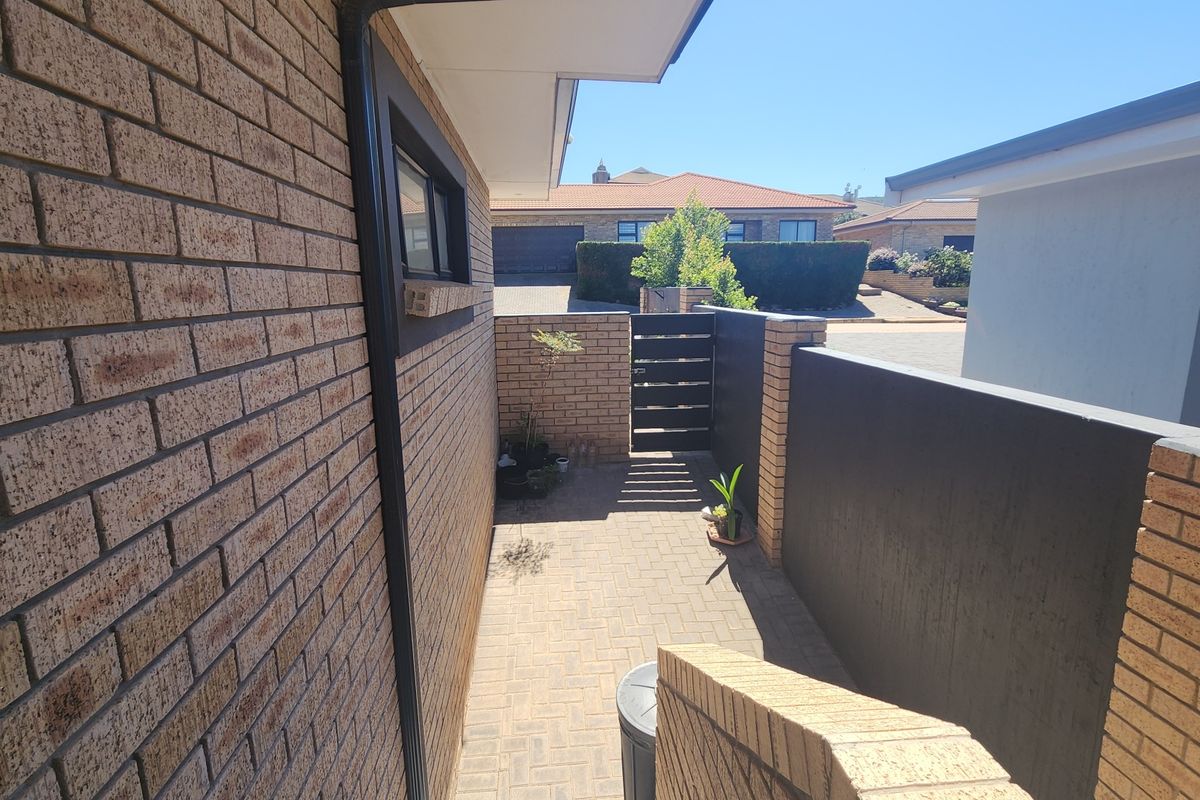 A side walkway featuring brick paving, enclosed by a face brick wall and a modern dark-painted boundary wall with a metal gate.