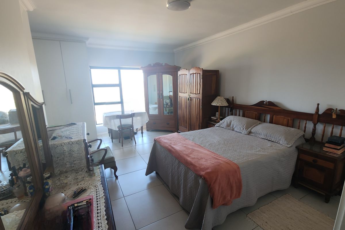 A spacious bedroom featuring tiled flooring, built-in cupboards, and classic cornicing, offering a functional layout with natural light.