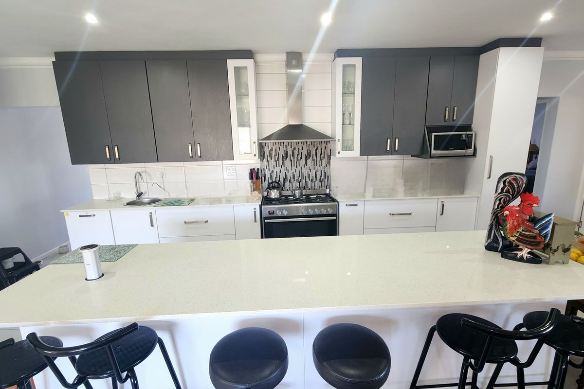 Modern kitchen featuring a large island, dual-tone cabinetry, quartz countertops, gas stove with extractor fan, and built-in microwave.
