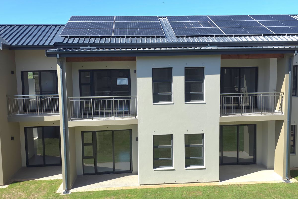A modern apartment building exterior featuring solar panels on the roof, private balconies, and ground-floor patio access with large sliding glass doors.