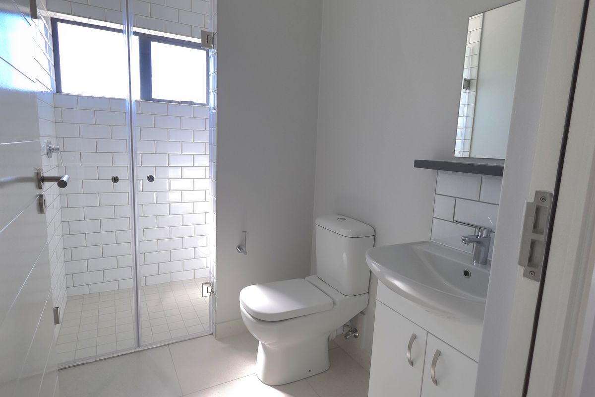 A modern bathroom featuring a glass-enclosed shower with subway tiling, a white vanity with basin, and a standard toilet.