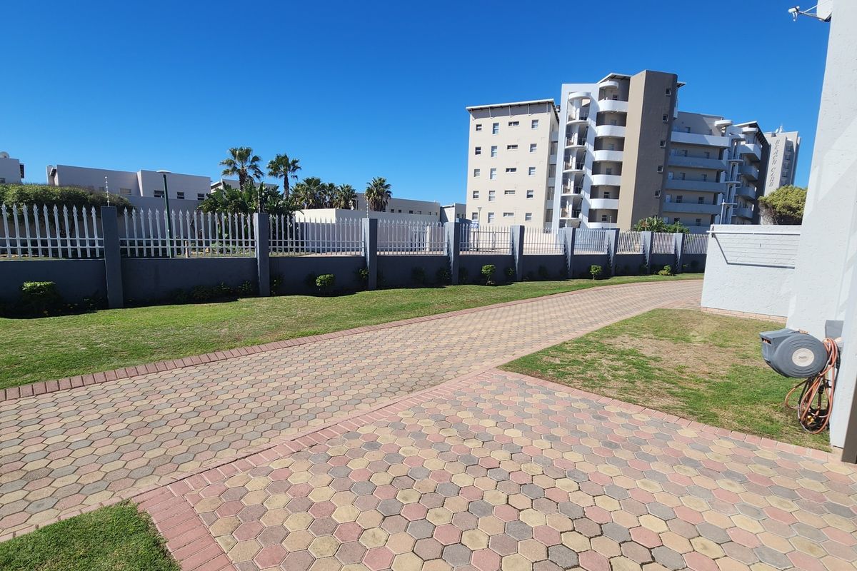 A view of the communal paved driveway and manicured lawn area within the townhouse complex, featuring perimeter walling and security fencing.