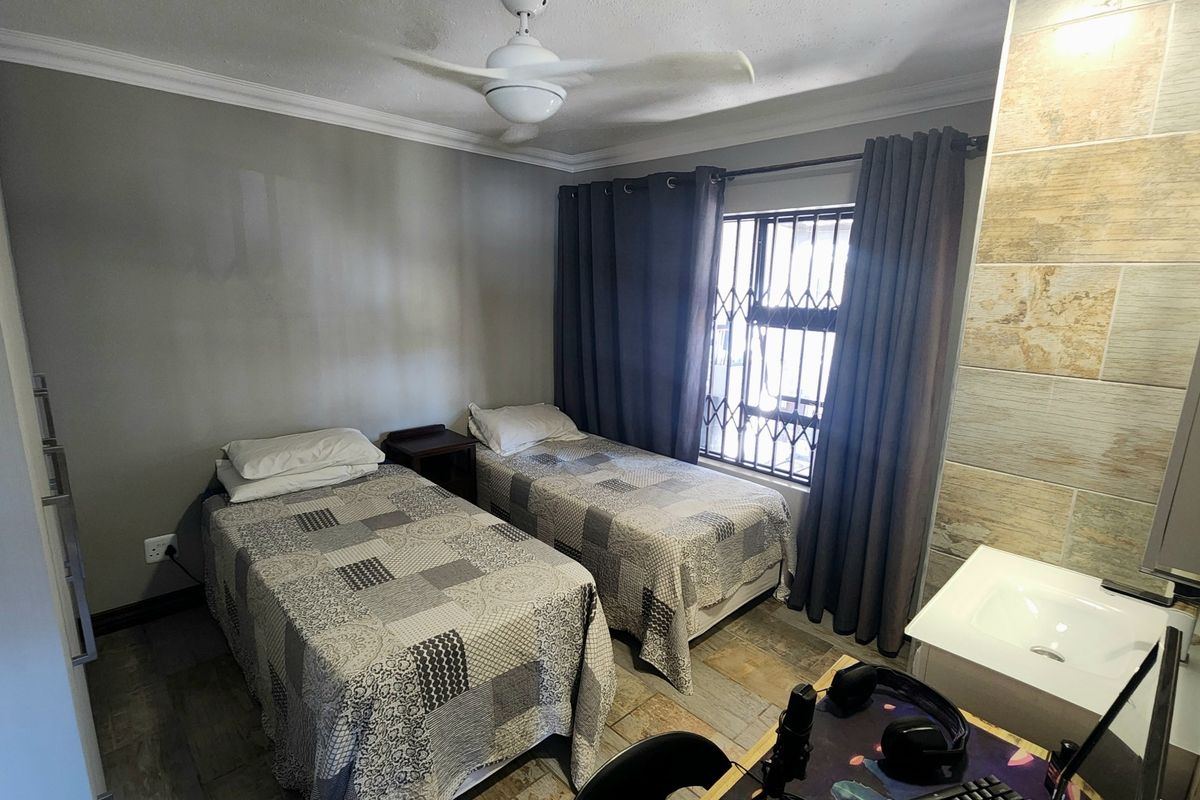 A bedroom featuring tiled flooring, a ceiling fan, and a built-in vanity basin area with stone-look wall tiling.