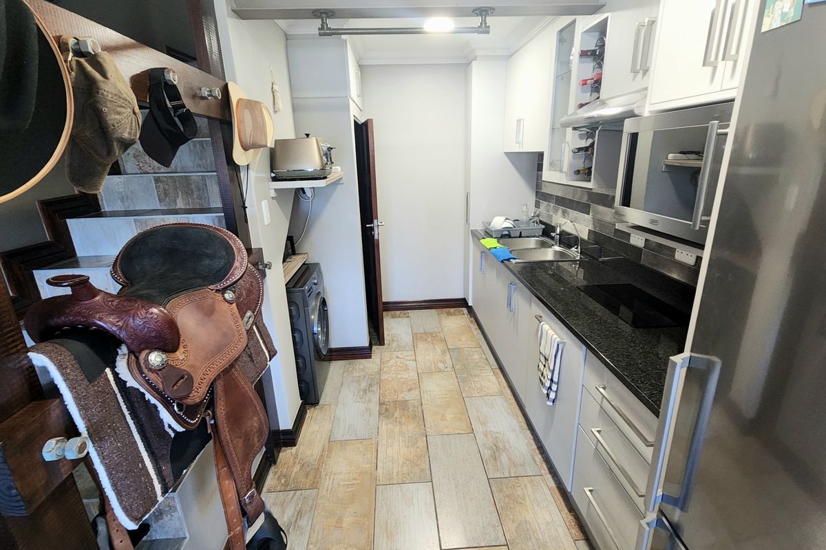 A functional galley-style kitchen featuring dark granite countertops, white cabinetry, a built-in oven, and tiled flooring.