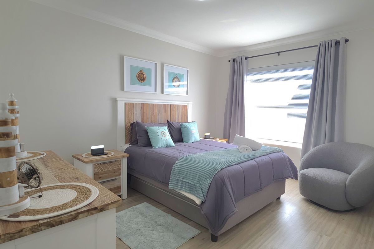 A well-maintained bedroom featuring light wood-look flooring, neutral wall tones, and a large window with curtain treatments.