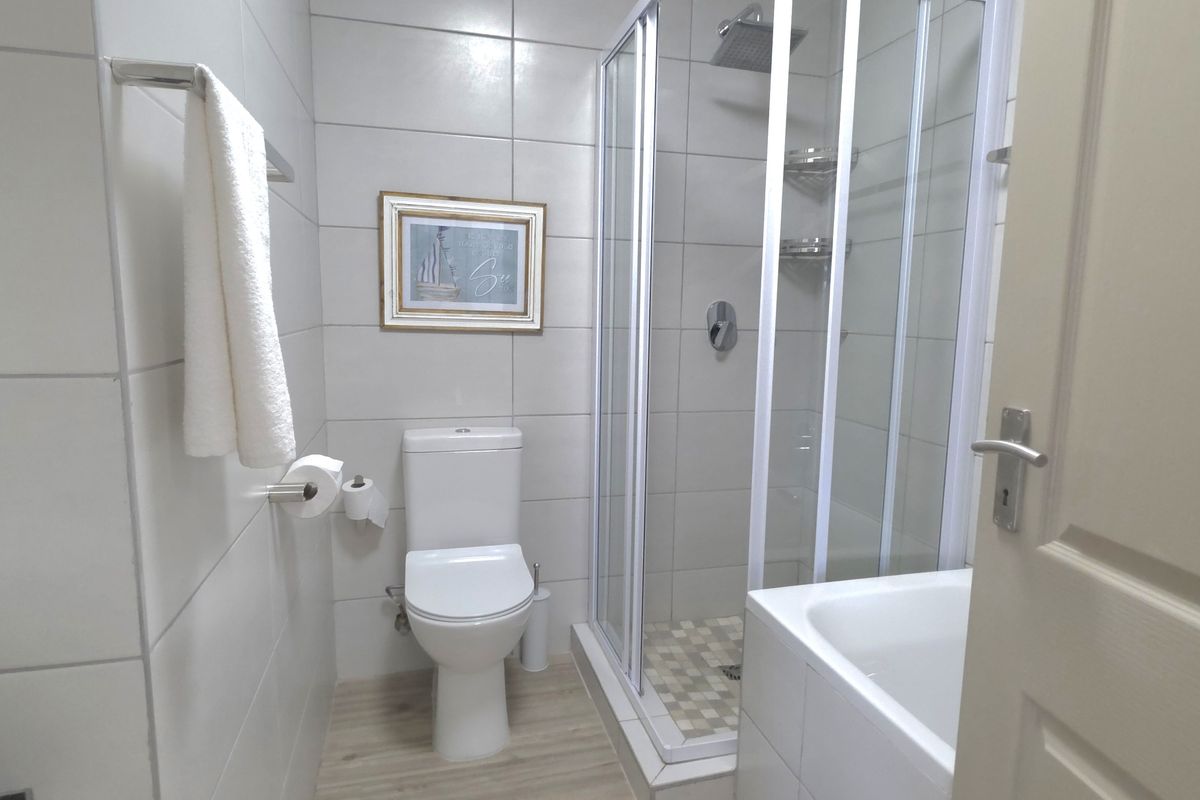 A clean, modern bathroom featuring a glass-enclosed shower, a white toilet, and neutral wall tiling.