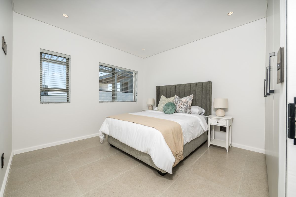 A modern, well-lit bedroom featuring neutral tiled flooring, recessed ceiling lighting, and built-in cabinetry.