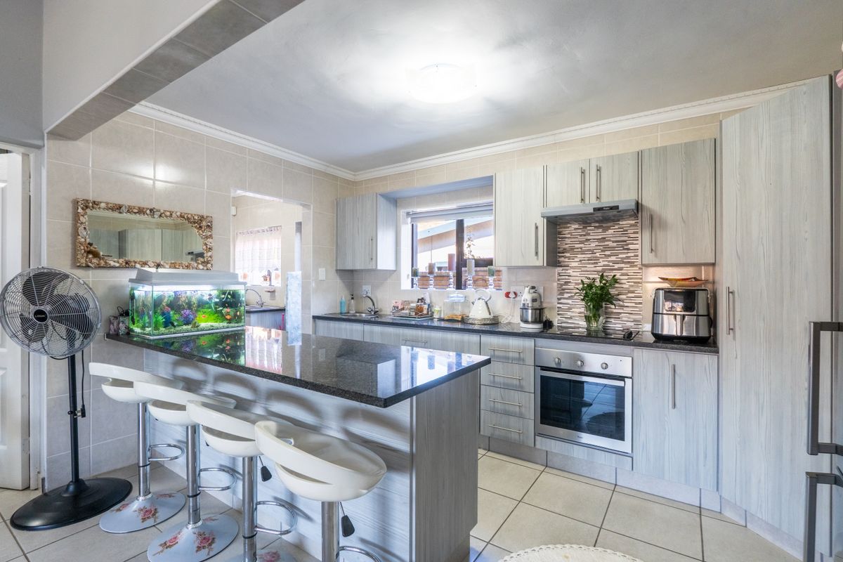 A functional kitchen featuring granite countertops, built-in cabinetry, a tiled backsplash, and integrated oven and hob, with an adjoining breakfast bar area.