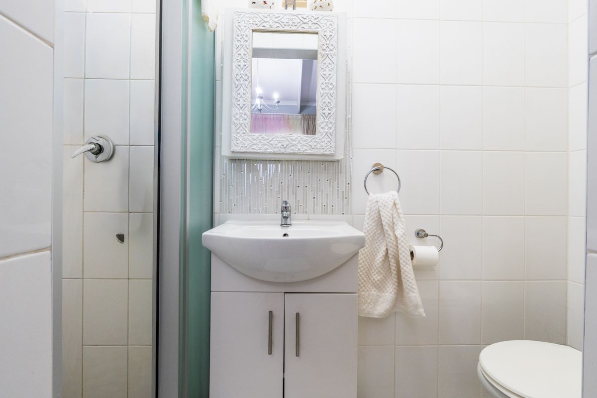 A compact bathroom featuring a white vanity cabinet, ceramic basin, tiled walls, and a shower enclosure.