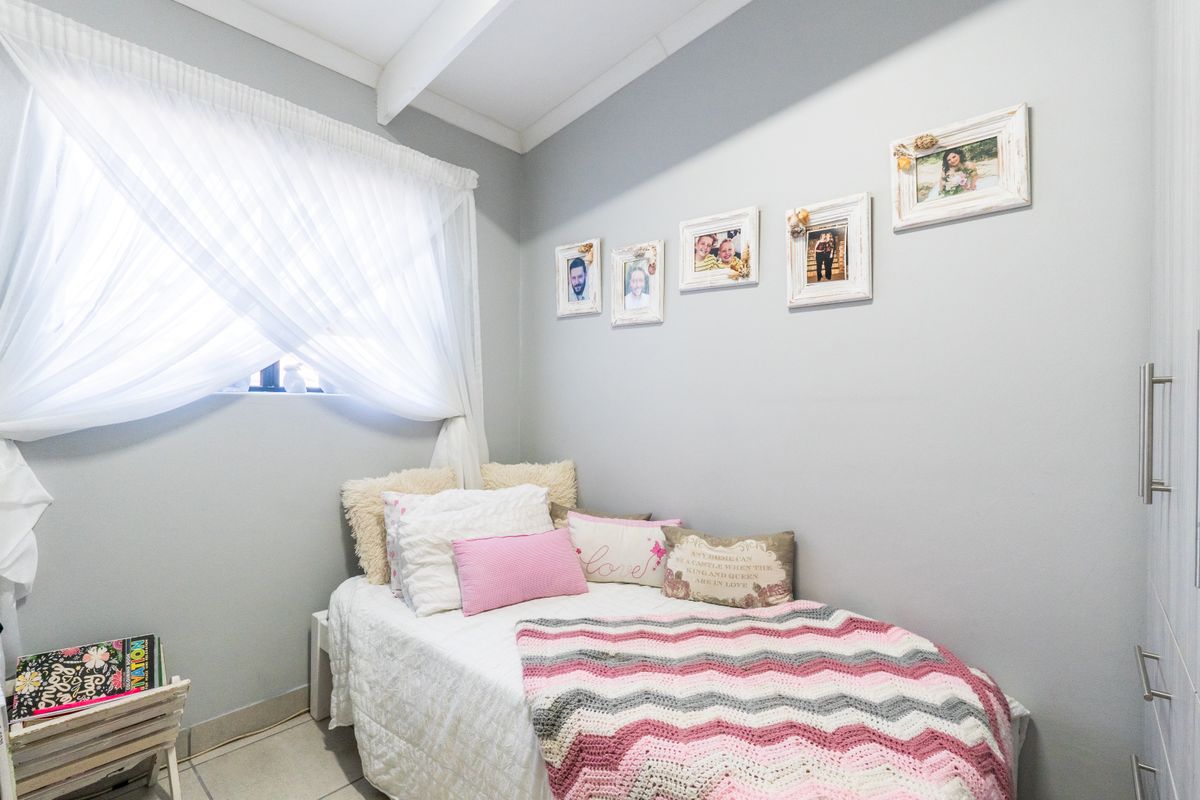 A cozy bedroom featuring neutral wall tones, tiled flooring, exposed ceiling beams, and built-in cupboard storage.
