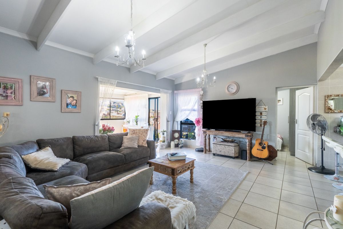 Spacious living room featuring vaulted ceilings with exposed beams, neutral tiled flooring, and large sliding glass doors providing access to the outdoor area.