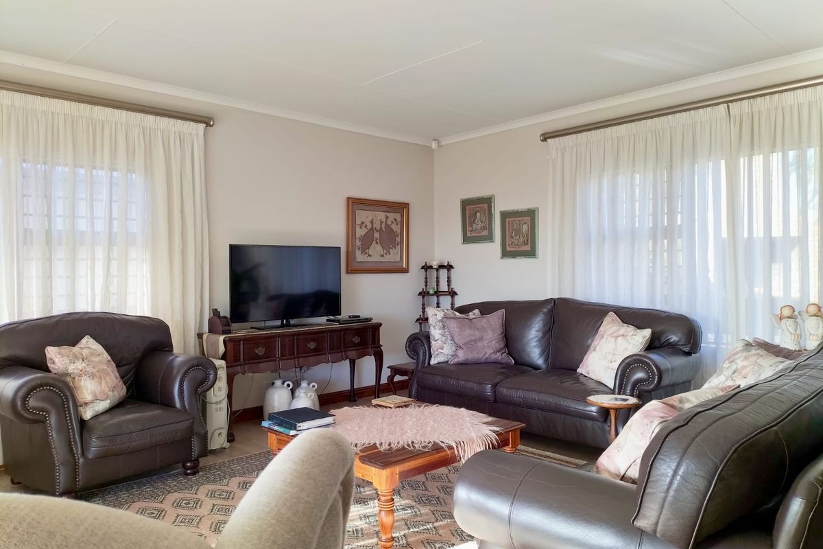 A comfortable living room featuring neutral wall tones, coved ceilings, and large windows with fitted curtain rods, providing a bright and inviting space.