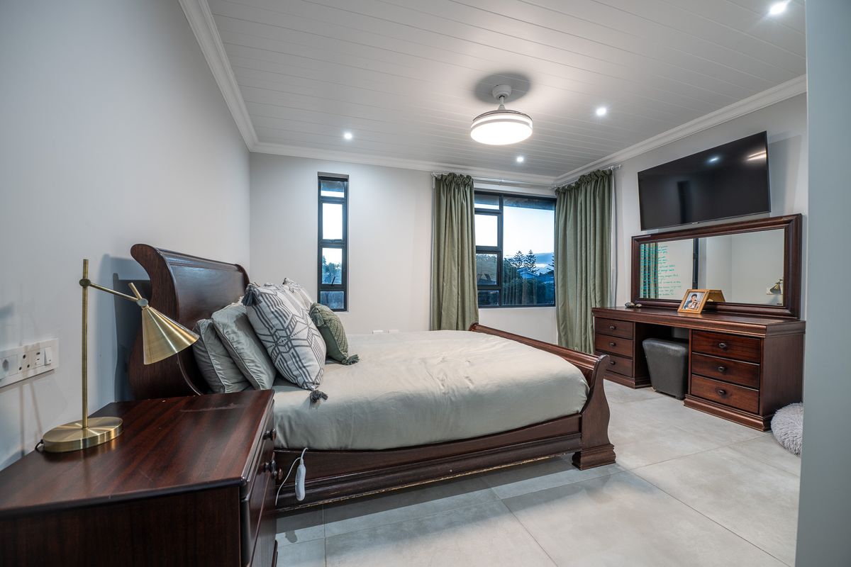 A well-maintained bedroom featuring tiled flooring, a tongue-and-groove ceiling with integrated lighting, and large windows providing natural light.