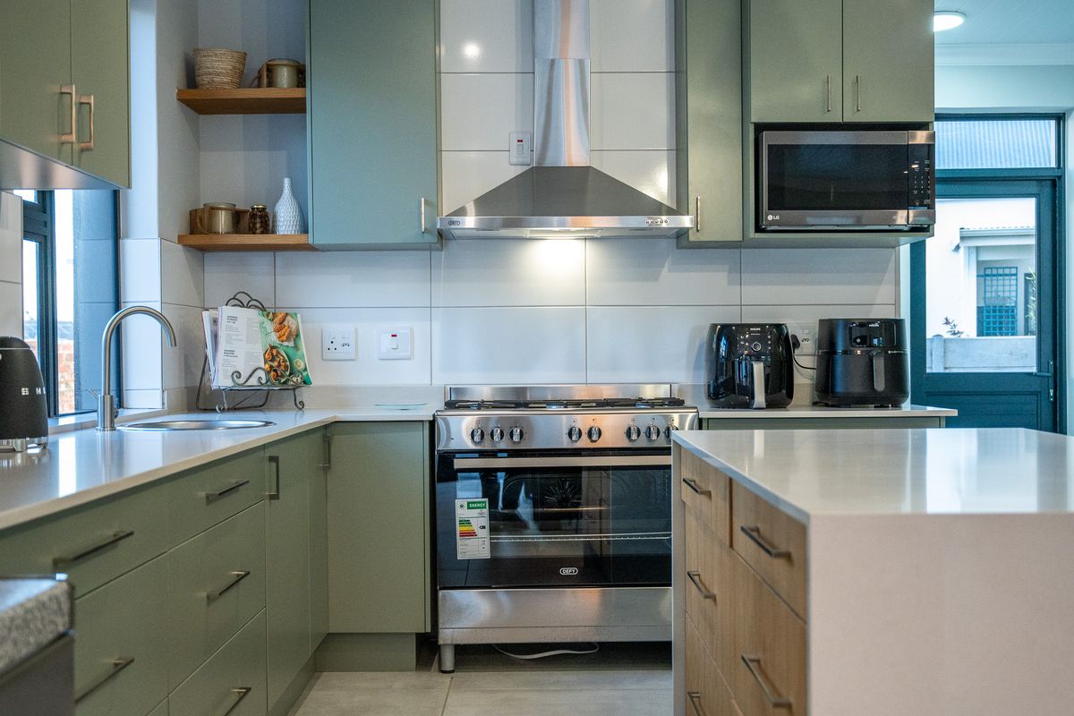 Modern kitchen featuring sage green cabinetry, stone countertops, stainless steel gas stove, extractor fan, and built-in microwave.