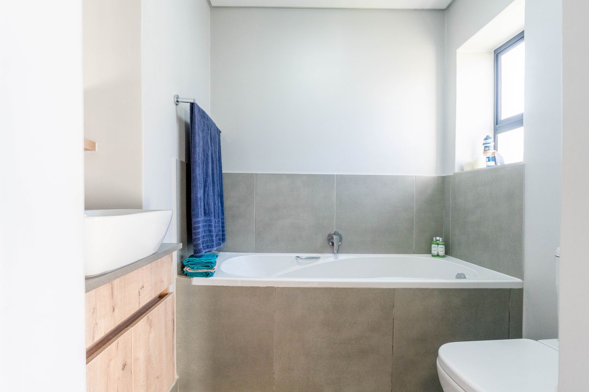 A modern bathroom featuring a built-in bathtub with grey tiled surround, a vanity with a vessel sink, and a window for natural light.