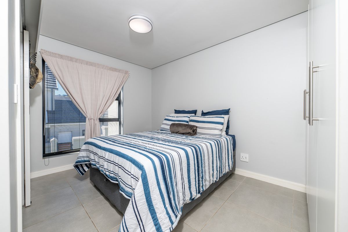 A well-maintained bedroom featuring neutral floor tiles, built-in cupboards, and a large window providing natural light.