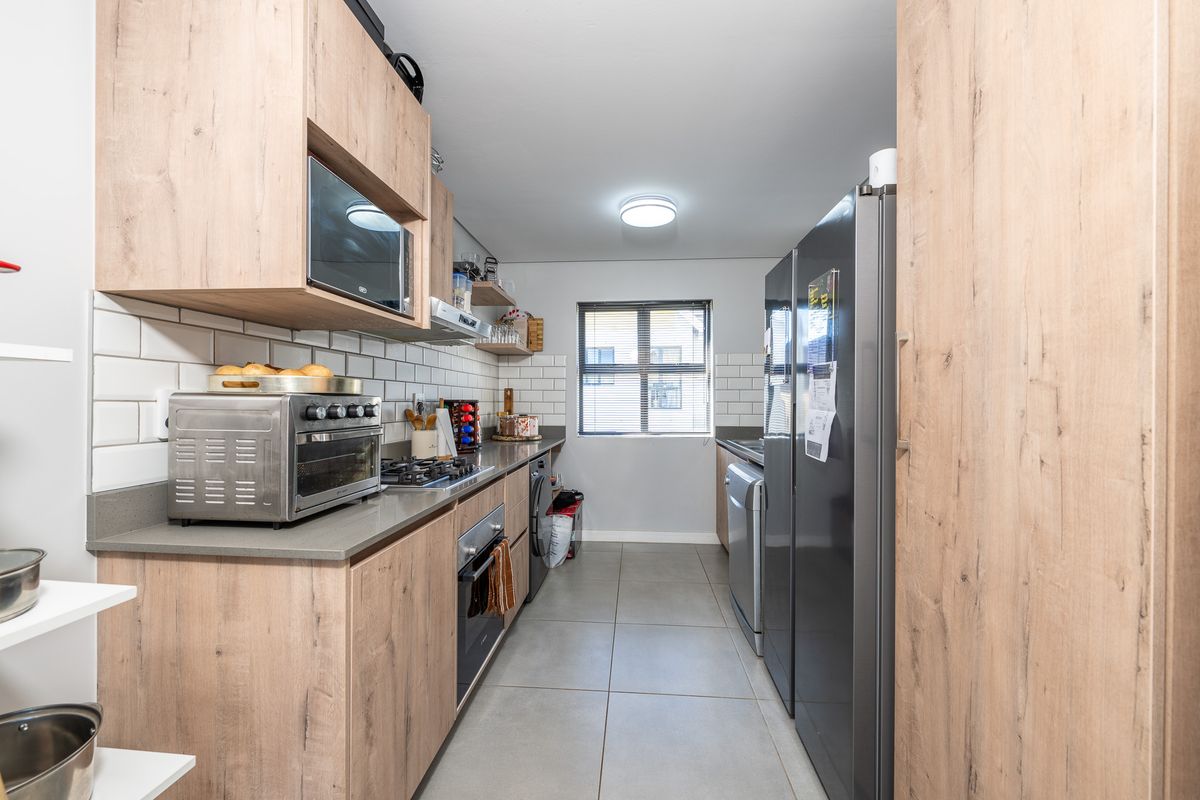 A modern galley-style kitchen featuring light wood-grain cabinetry, stone-look countertops, subway tile backsplash, and integrated stainless steel appliances.