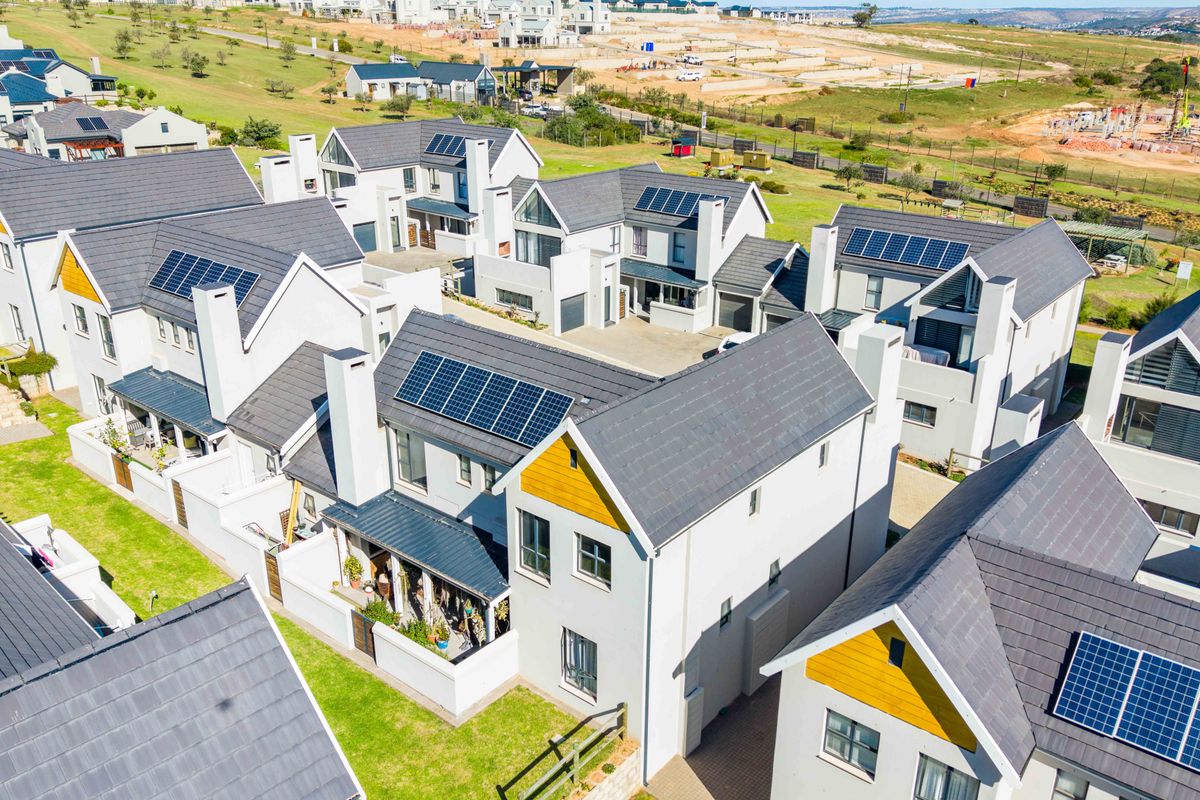Aerial view of a modern townhouse complex featuring pitched tiled roofs, solar panel installations, and landscaped garden areas within a residential estate.