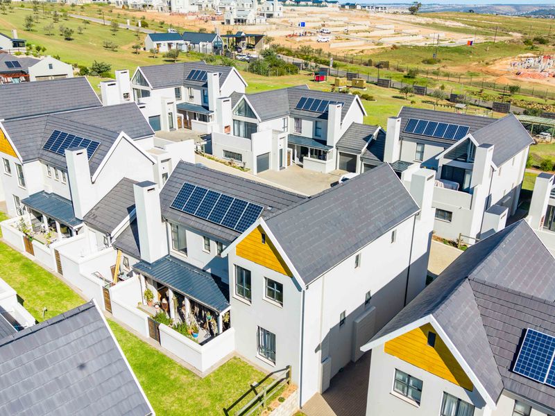 Aerial view of a modern townhouse complex featuring pitched tiled roofs, solar panel installations, and landscaped garden areas within a residential estate.