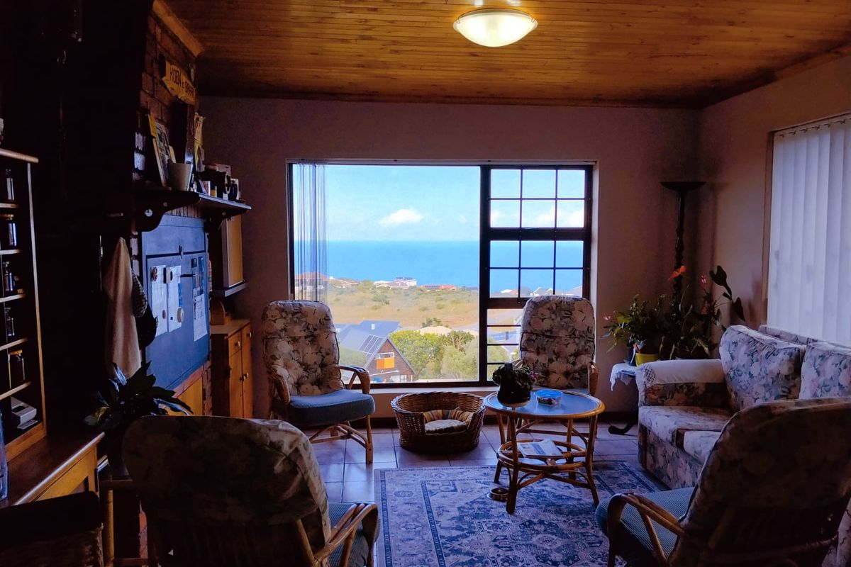 A cozy living room featuring a large window with scenic ocean views, a brick fireplace surround, and a warm timber-paneled ceiling.