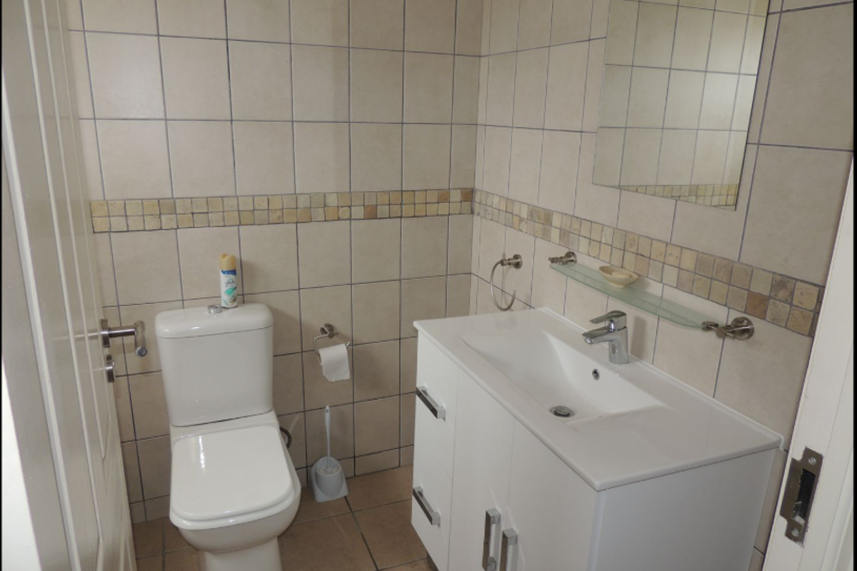 A compact bathroom featuring a white vanity with integrated basin, a modern toilet, and neutral wall tiling with a decorative mosaic border.