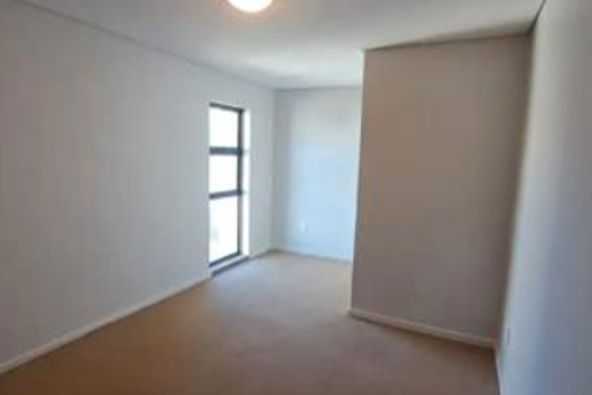 A bright, empty bedroom featuring neutral carpeting and a large window, providing a clean and versatile space ready for personalization.