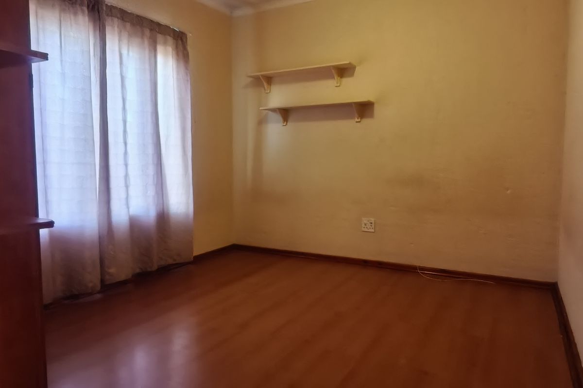 A vacant bedroom featuring laminate flooring, built-in wooden shelving, and a window with curtains.