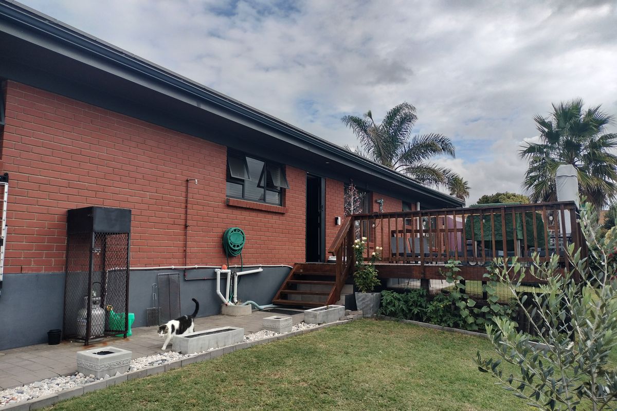 Rear view of the property featuring a red brick facade, raised timber deck with stairs, and a paved patio area leading to the garden.