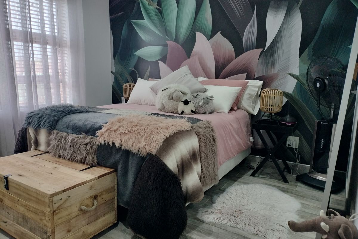 A well-maintained bedroom featuring a striking botanical feature wall, wood-look tiled flooring, and modern window blinds.