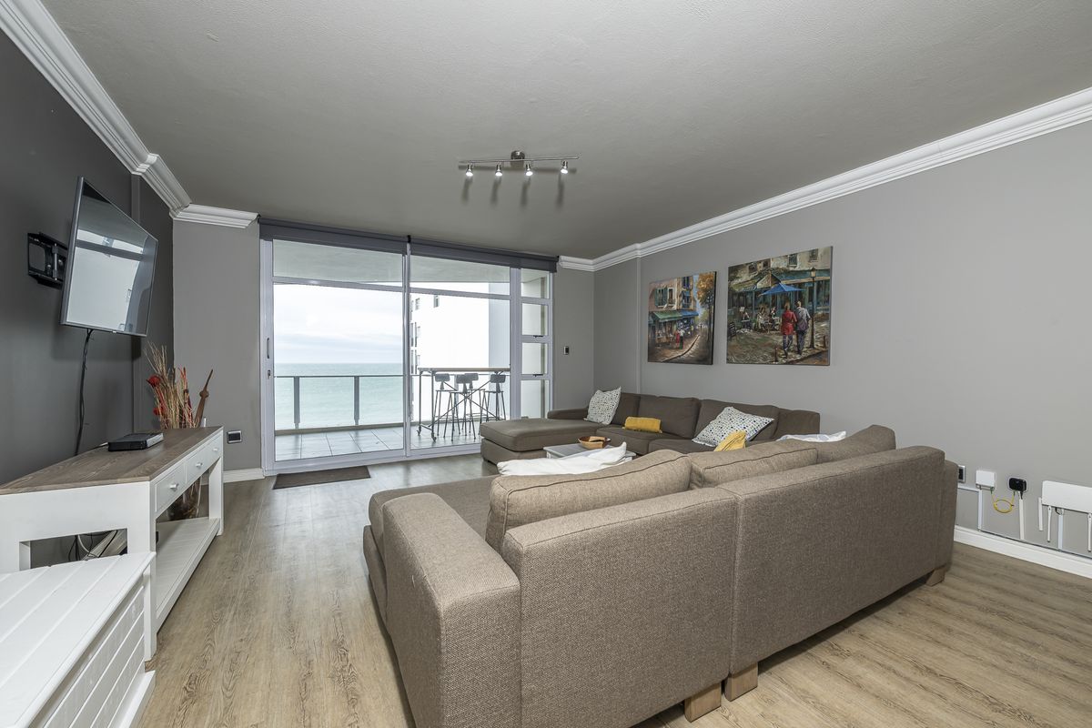 Spacious living room featuring laminate flooring, crown molding, and large sliding glass doors that open to a balcony with ocean views.