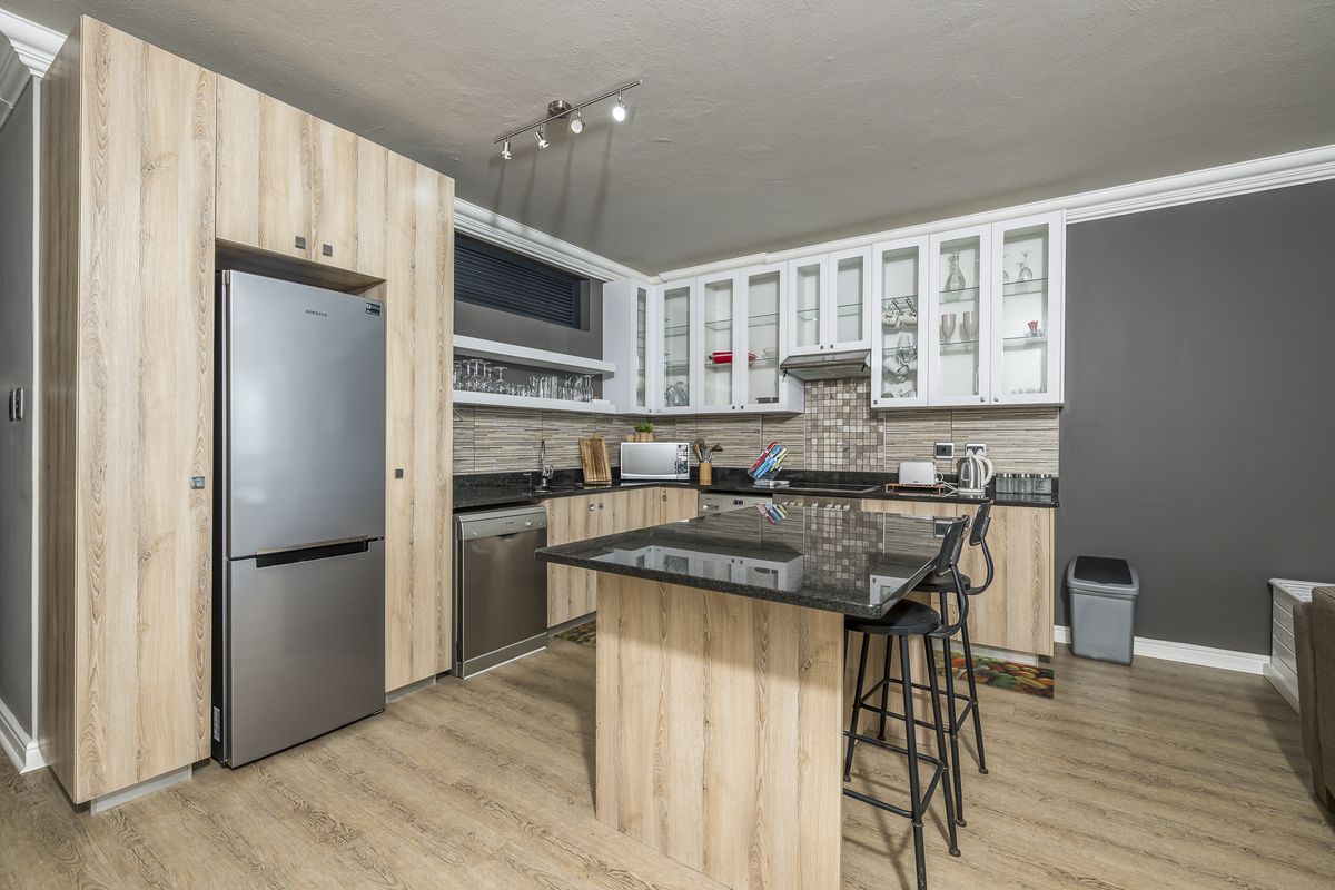 Modern kitchen featuring light wood-grain cabinetry, granite countertops, a central island, and a tiled backsplash with integrated extractor fan.