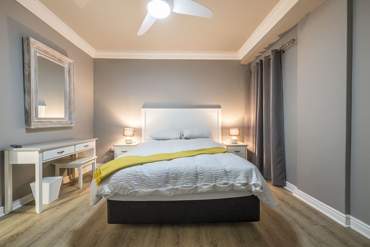 A well-maintained bedroom featuring light wood-look laminate flooring, crown molding, and a ceiling fan, creating a comfortable and neutral living space.