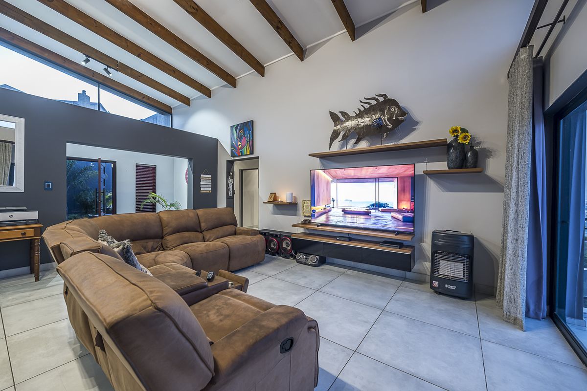 Spacious living room featuring high vaulted ceilings with exposed timber beams, large clerestory windows, tiled flooring, and direct access to outdoor areas via sliding doors.