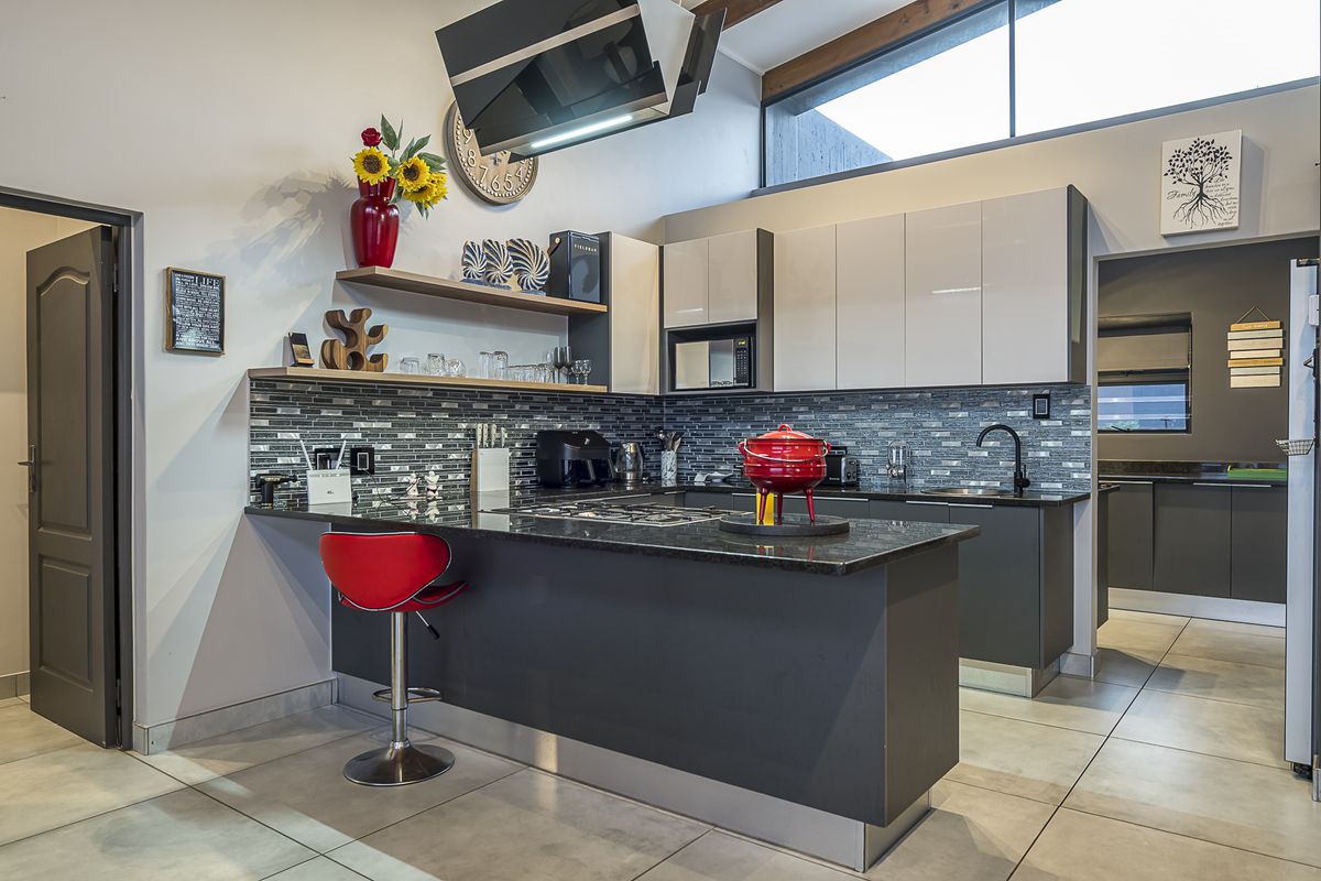 Modern kitchen featuring high-gloss cabinetry, granite countertops, a gas hob with extractor fan, and a stylish mosaic tile backsplash.