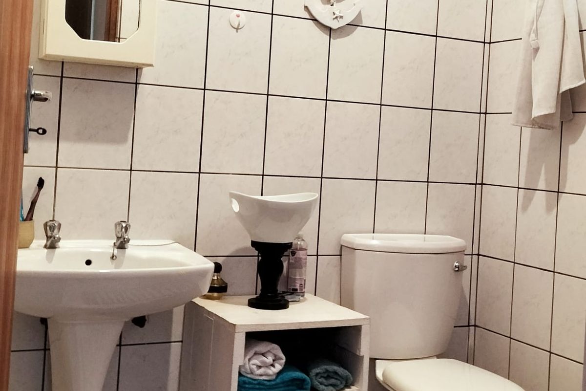 A functional bathroom featuring a pedestal basin, standard toilet, and full-height wall tiling.