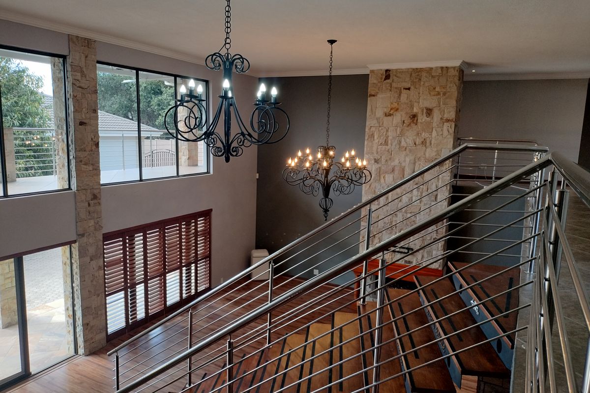 Spacious living area featuring a double-volume ceiling, stone-clad feature wall, timber staircase with stainless steel balustrades, and large windows with wooden shutters.