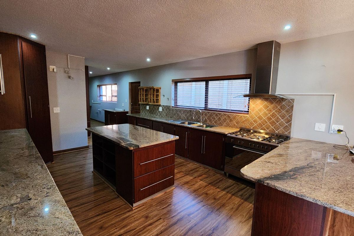 Spacious kitchen featuring dark wood cabinetry, granite countertops, a central island, and a stainless steel gas stove with a matching extractor fan.
