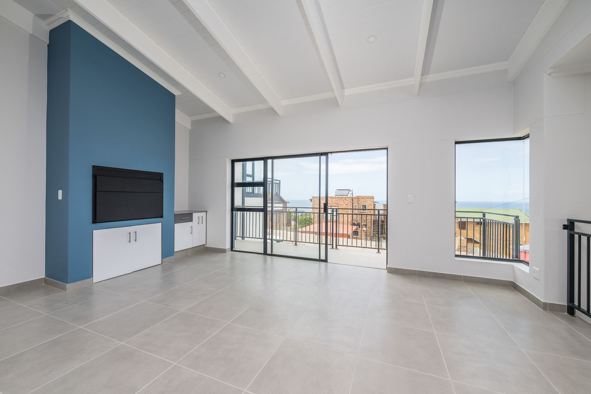 Bright and spacious living area featuring high vaulted ceilings, tiled flooring, built-in cabinetry, and large sliding doors opening to a balcony with coastal views.